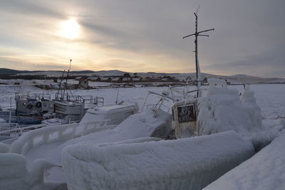 Snow covered boats on land against sky during sunset