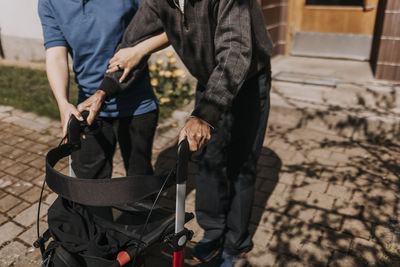 Midsection of female care assistant supporting senior man with walker