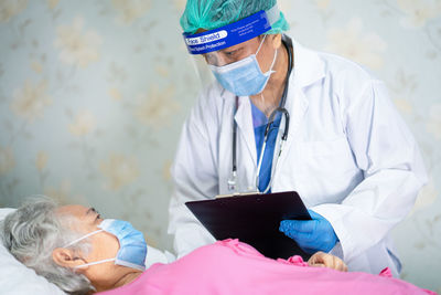 Doctor wearing flu mask and face shield examining patient in hospital