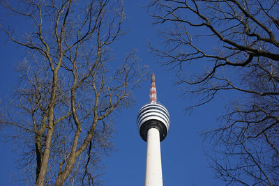 Low angle view of fernsehturm stuttgart amidst bare trees against blue sky