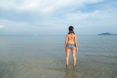 Rear view of young woman standing at beach against sky