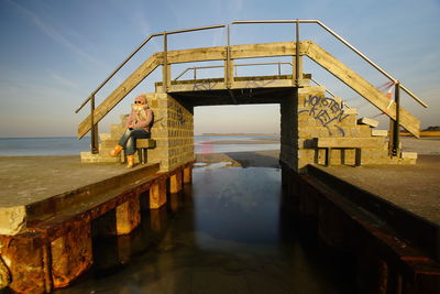 Woman sitting on pier over sea against sky