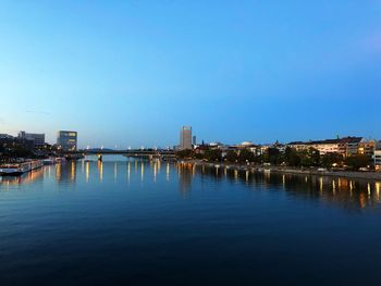 River by illuminated buildings against clear sky at dusk