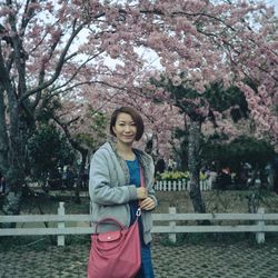 Portrait of smiling woman standing against cherry blossoms on tree 