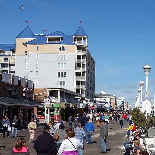 building exterior, architecture, large group of people, built structure, city, person, street, city life, men, lifestyles, crowd, clear sky, walking, leisure activity, mixed age range, sunlight, day, city street, building