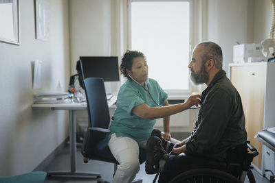 Female doctor examining mature man with disability in hospital