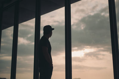 Silhouette man standing by window against sky