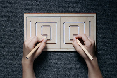 Child hands holding pencils and drawing lines in two-sided wooden stencil labyrinth