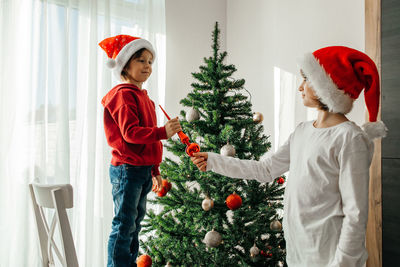 Children in red santa claus hats decorate the christmas tree for the holiday. eve of new year 