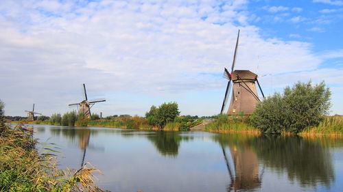 Traditional windmill by lake against sky