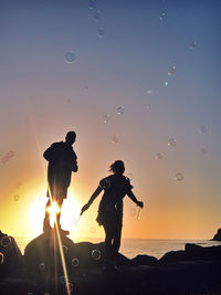 Silhouette people standing on shore against sky during sunset