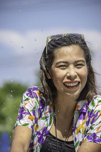 Portrait of smiling woman splashing water against sky