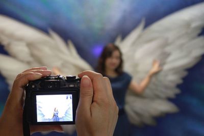 Cropped image of hands photographing woman wearing wing costume