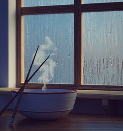 Chopsticks and bowl on table by window at home