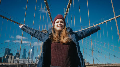 Smiling young woman standing against bridge against sky