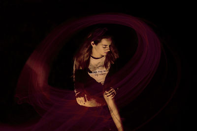 Young woman looking away while standing against black background