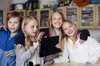 Portrait of friends with girl using tablet in classroom