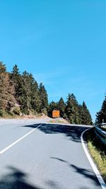 Road by trees against blue sky