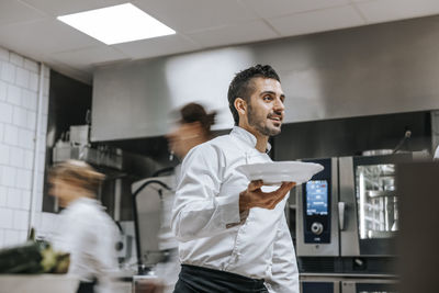 Young male chef carrying food plate in kitchen at restaurant