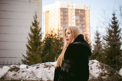 Thoughtful woman in warm clothing against buildings