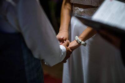 Midsection of groom holding hands of bride during wedding
