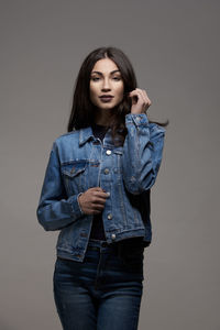 Portrait of young woman standing against gray background