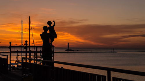 Silhouette man with daughter on pier by sea during sunset