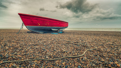 Red boat moored on beach against sky