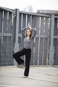 Young woman meditating with arms raised against metal structure