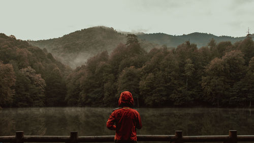Rear view of man standing by lake against mountain