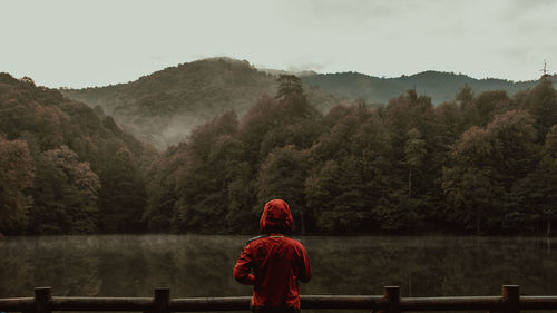 Rear view of man standing by lake against mountain