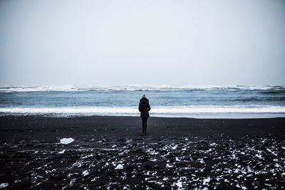 Rear view of man standing on beach against clear sky