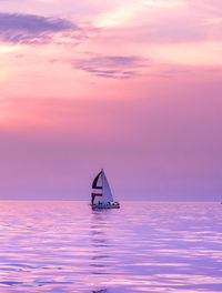 A lone sail boat floats on a still lake with a beautiful sunset of purple and pink