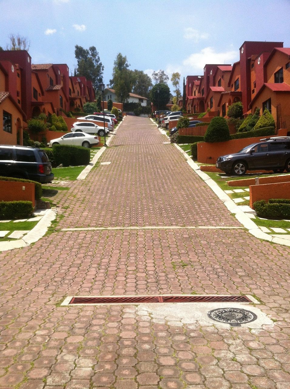 building exterior, architecture, built structure, street, the way forward, cobblestone, house, city, residential building, sky, transportation, road, residential structure, diminishing perspective, outdoors, car, day, building, tree, vanishing point