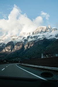 Road amidst snowcapped mountains against sky seen through car windshield