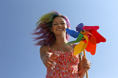 Happy woman holding colorful pinwheel toy gesturing under blue sky