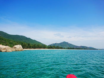 Low section of person by sea against blue sky