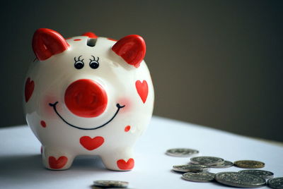 Close-up of coins with piggy bank on table against wall