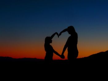 Silhouette mother and daughter making heart shape from hands at desert during sunset