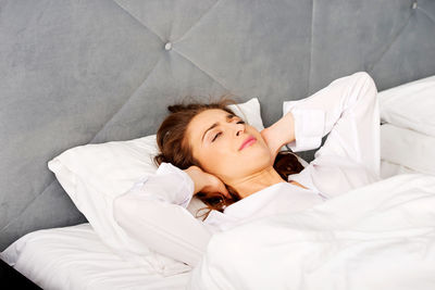 Young woman with hands covering ears lying on bed at home