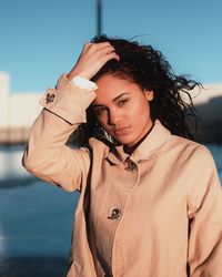 Portrait of young woman with hand in hair standing against sky