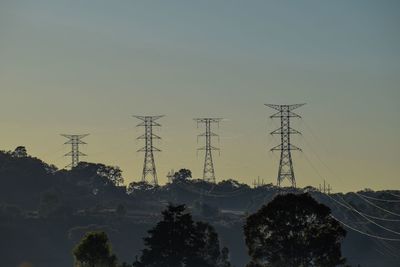 Silhouette trees and electricity pylon against sky during sunset