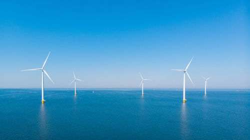 Windmills on field against clear blue sky