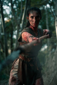 Brave female in viking costume standing while outstretching hand with spear during battle in woods