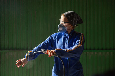 Concentrated female mechanic in uniform and mask checking air compressor gun before work