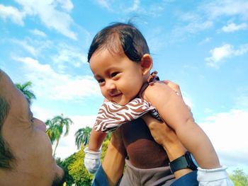 Father carrying son against sky