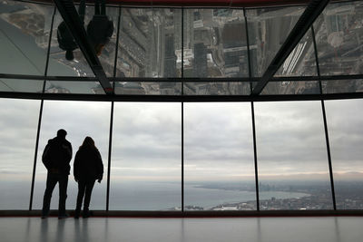 Rear view of people on glass window against sky