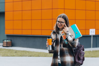 Young woman using phone while standing against yellow wall