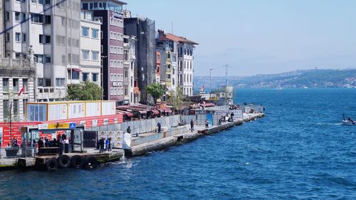 Boats in sea by buildings against sky in city