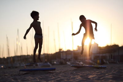 Silhouette men with arms raised against sky during sunset